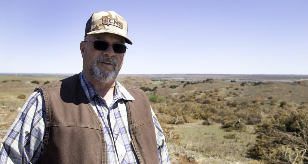 Jimmy Emmons talks about redcedar encroachment on a hill at his ranch near Leedey, where acres of trees have been cut by a mulching company. Photo by Kelly J Bostian / KJBOutdoors