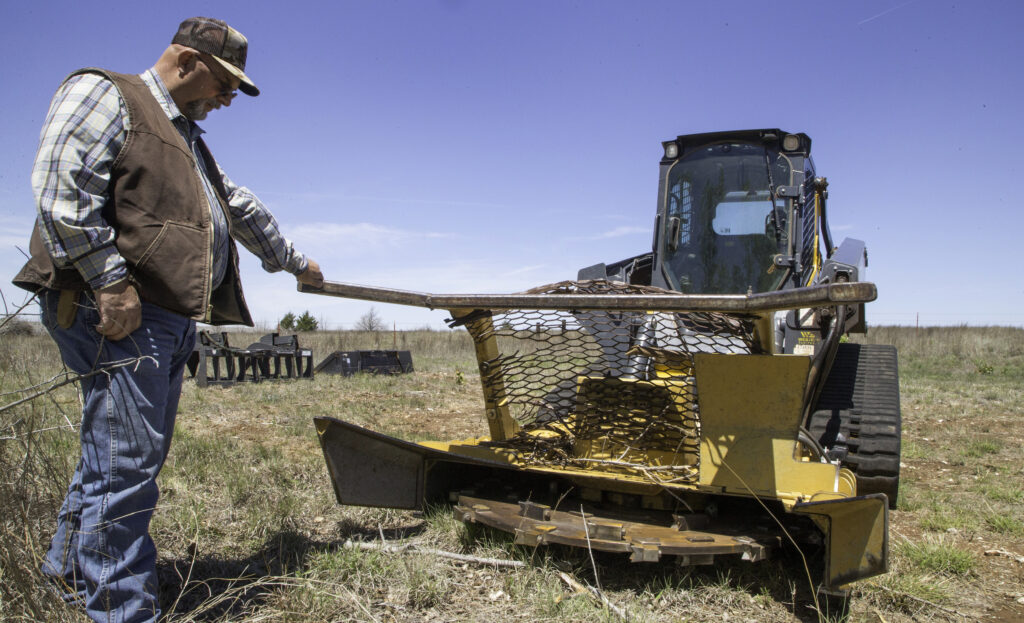 Jimmy Emmons explains the workings of a mulching attachment he uses to take down old stands of burned redcedar at his ranch near Leedey. Photo by Kelly J Bostian / KJBOutdoors